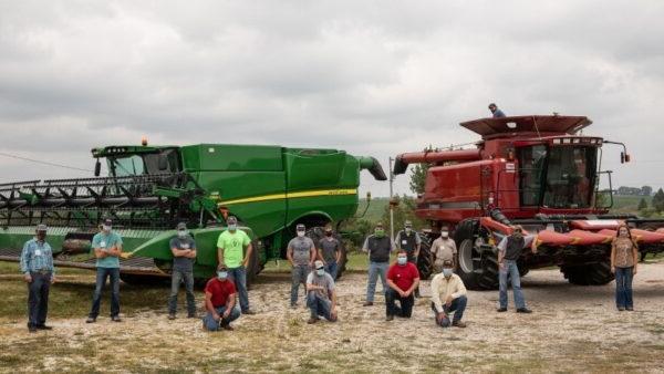 people in masks in front of farming equipment